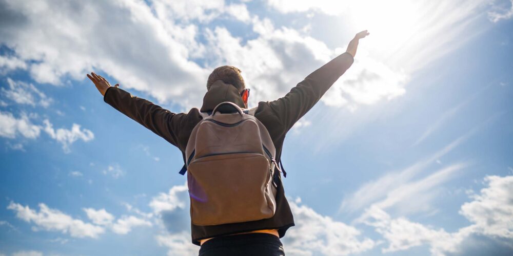 En person som sträcker upp armarna mot en blå himmel.