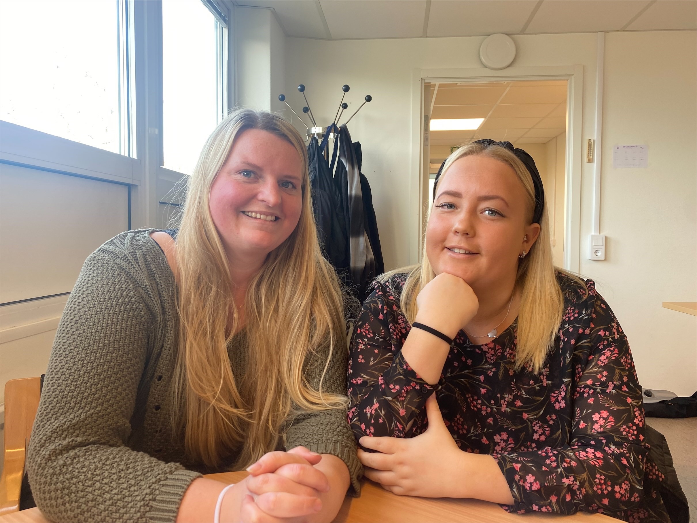 Två personer som ler. Båda två har blont hår. De sitter ner runt ett bord.