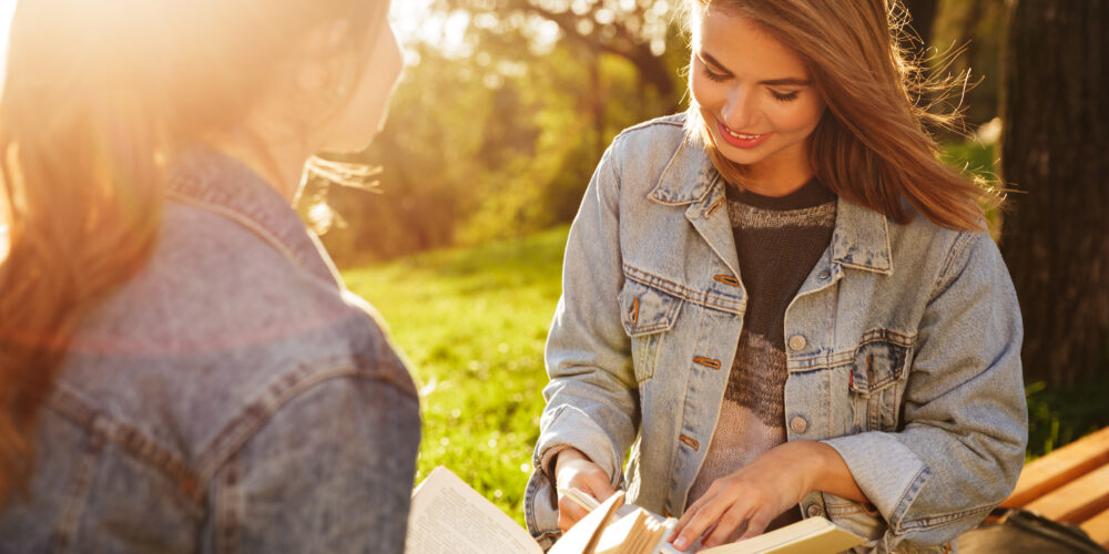 Närbild av två tjejer som läser böcker i parken en solig dag.