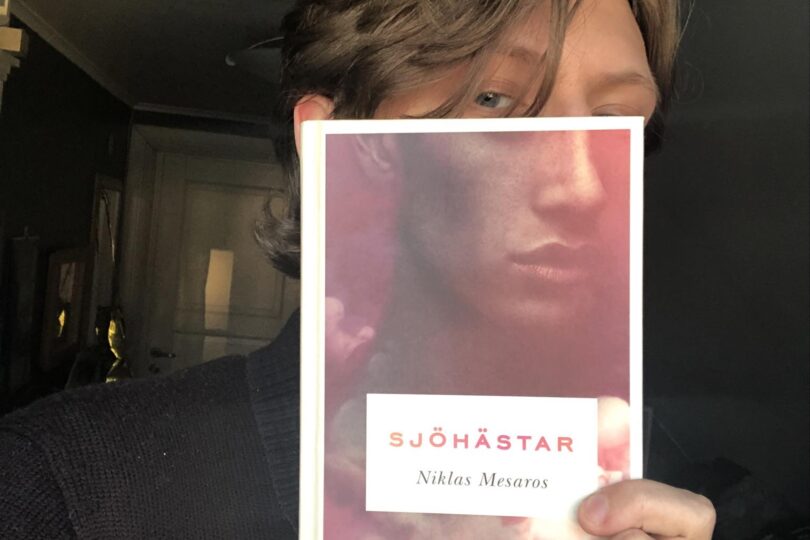 Elias håller en bok framför ansiktet. Bokens omslag är en siluett av ett annat ansikte.