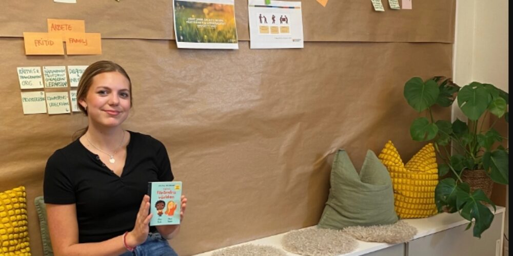 Evelina som sitter ner på en bänk. Hon håller i en bok där det står hur vi förändrar världen.