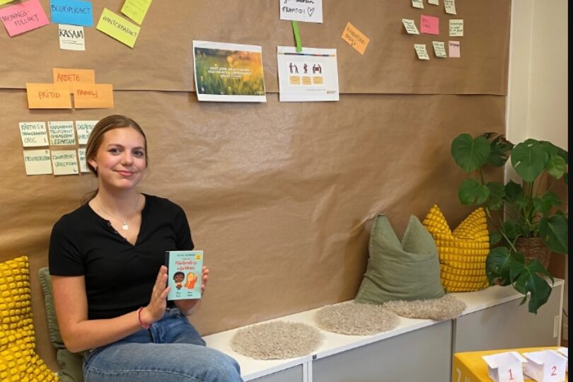 Evelina som sitter ner på en bänk. Hon håller i en bok där det står hur vi förändrar världen.