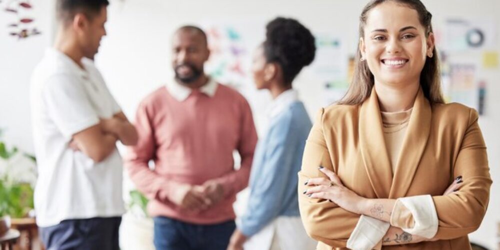 visar en person som korsar armarna. I bakgrunden står en grupp och diskuterar.