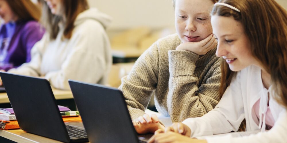 Två elever sitter i ett klassrum med sina skoldatorer
