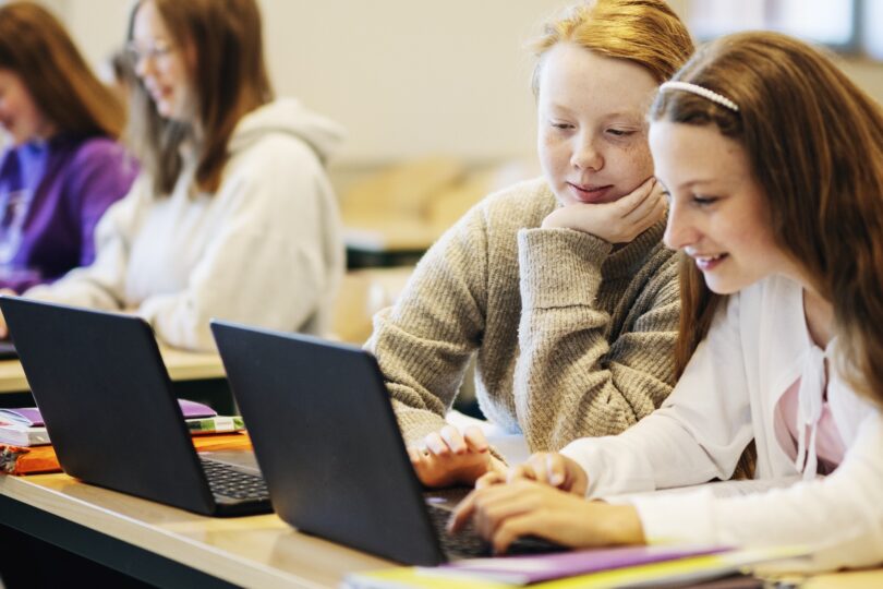 Två elever sitter i ett klassrum med sina skoldatorer