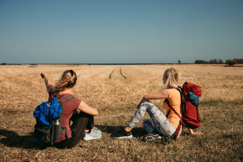 Två unga tjejer sitter med vandringsväskor på ett fält längs med Mörbylångaleden.