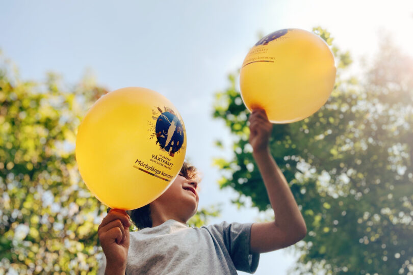 Ett barn håller i ballonger med Mörbylånga kommuns visionssymbol på