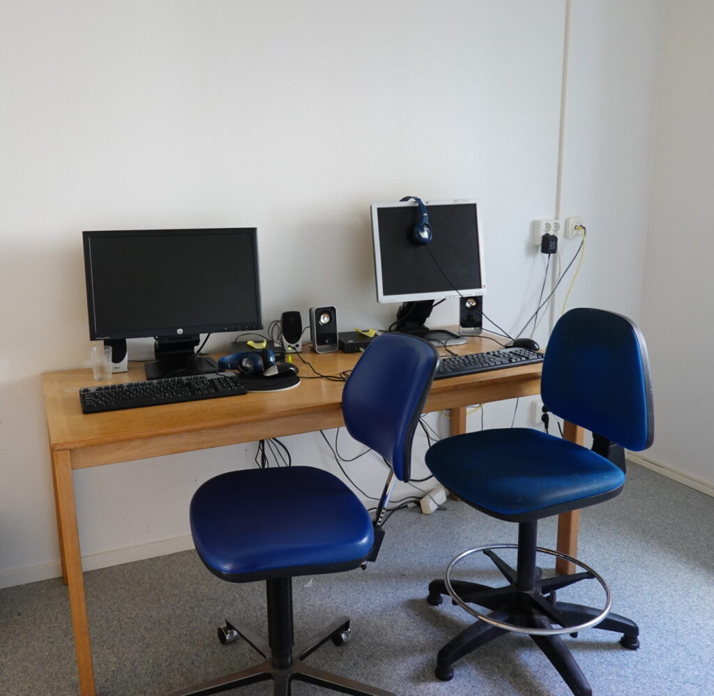 Bord med två datorer och två blåa kontorsstolar intill.