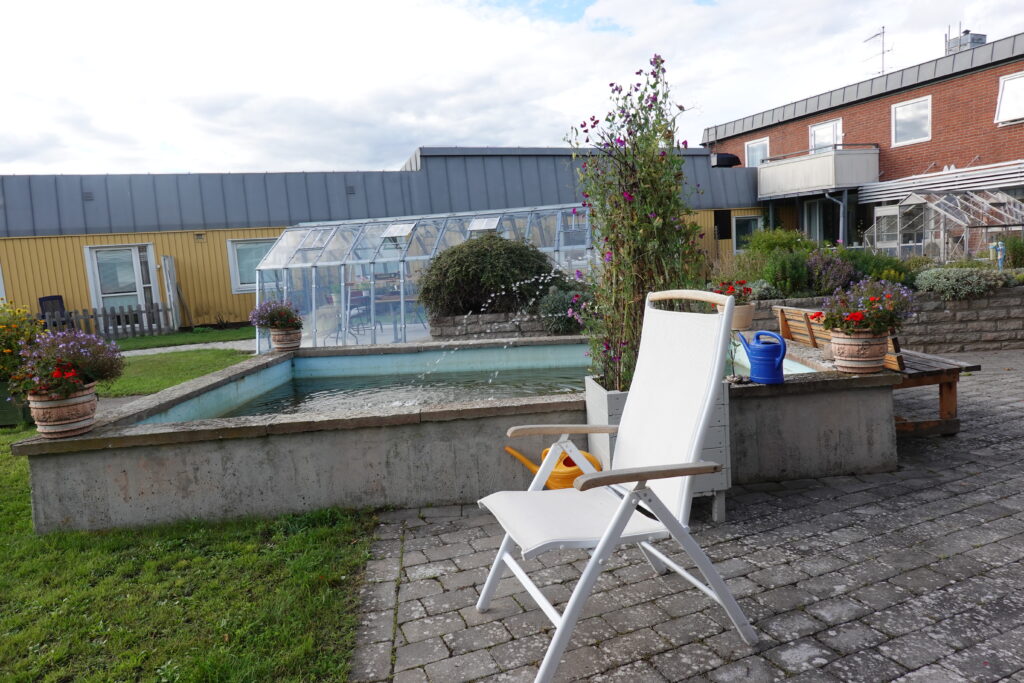 En stol framför fontän med växthus i bakgrunden