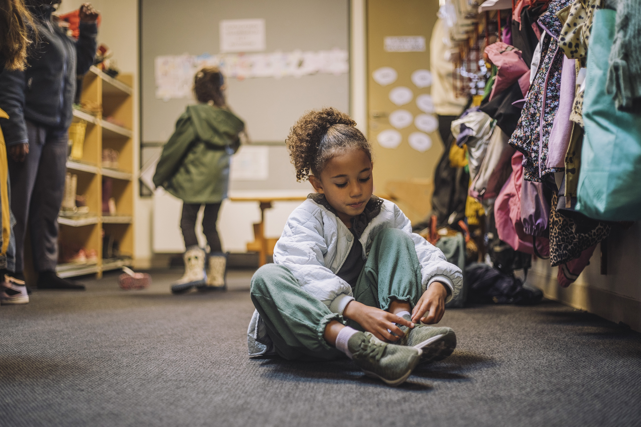 Ett barn i fyraårsåldern sitter på golvet på förskolan och knyter sina skor.