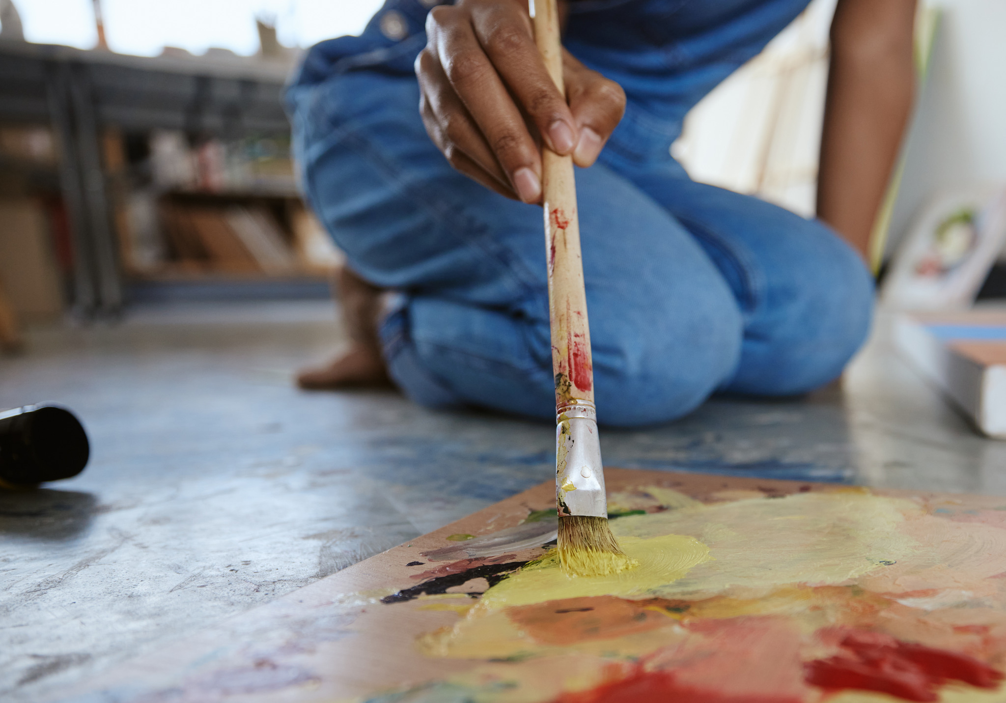 Ung person sitter på golvet och målar en tavla