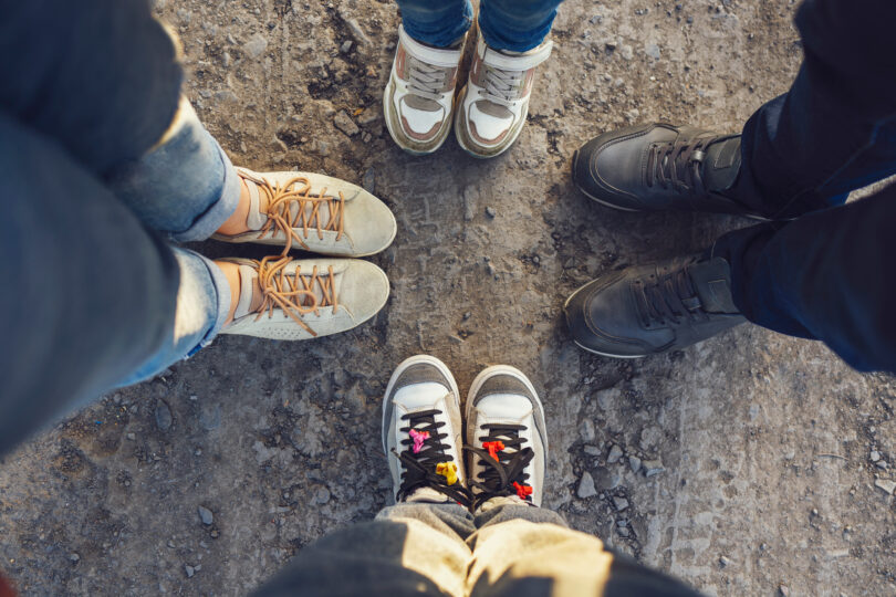 Fyra personer står i en cirkel, bilden är tagen uppifrån och visar deras skor på en grusig väg.