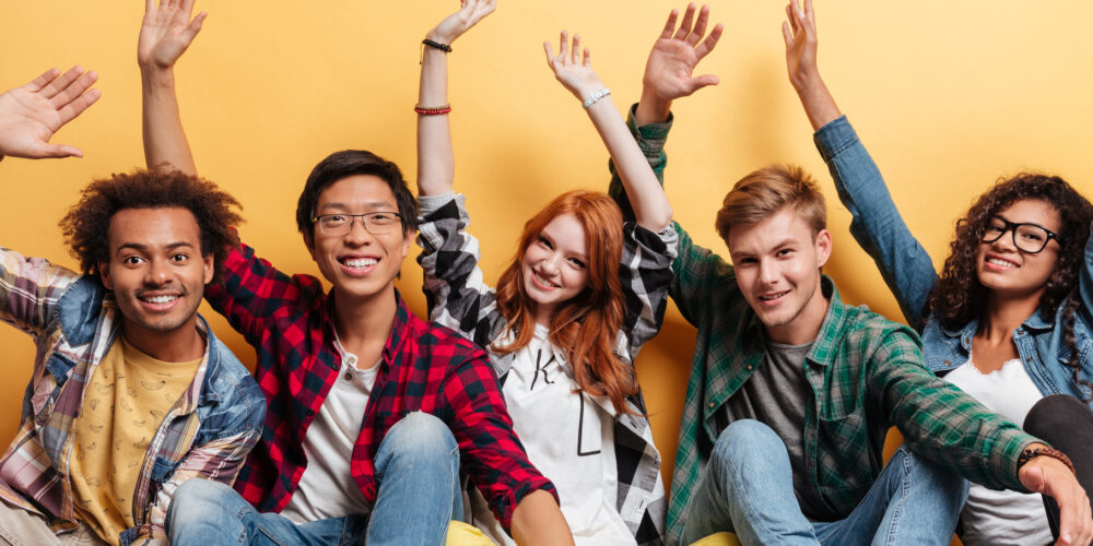 fem ungdomar sittandes på golvet med armarna i luften