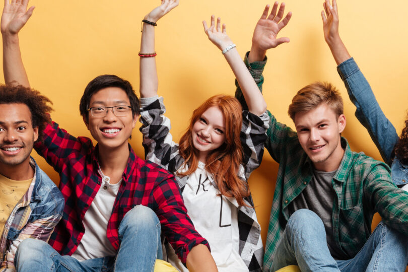 fem ungdomar sittandes på golvet med armarna i luften