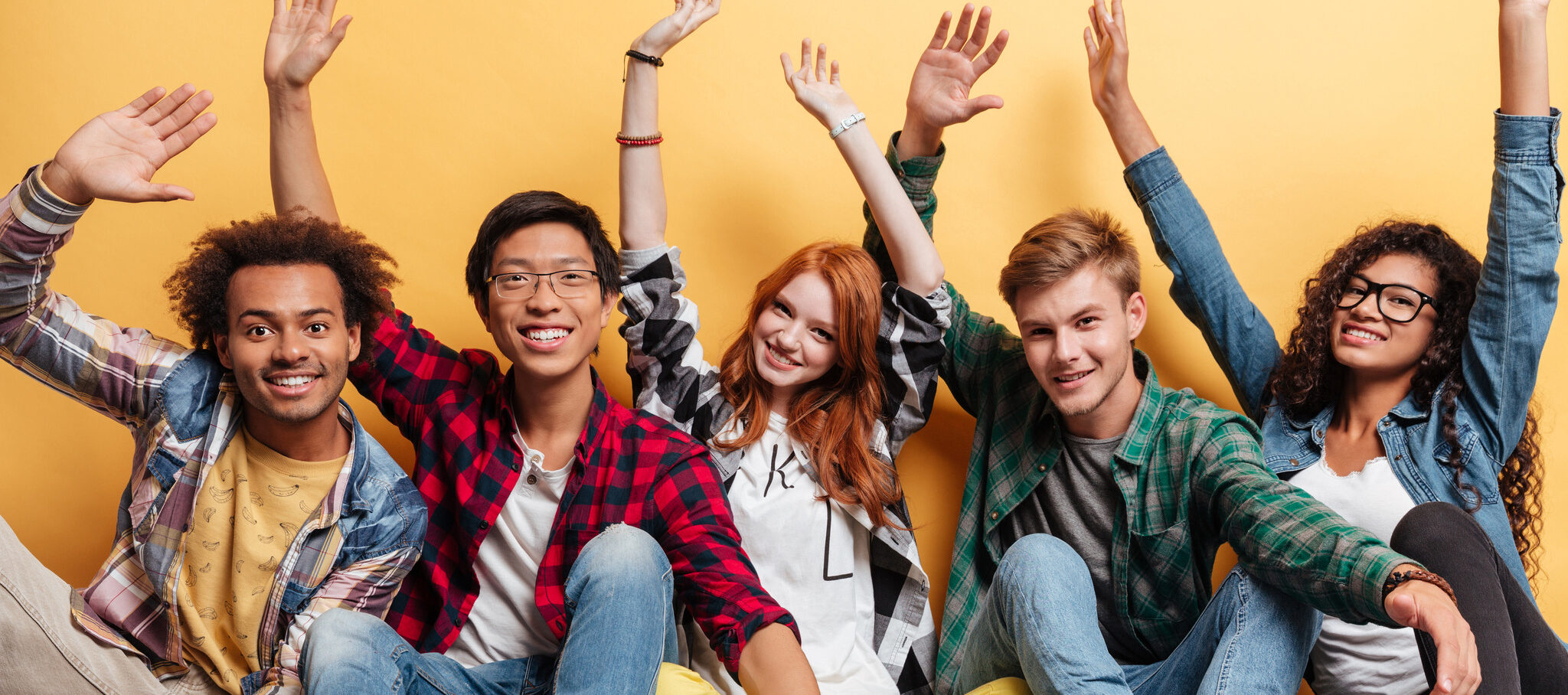 fem ungdomar sittandes på golvet med armarna i luften