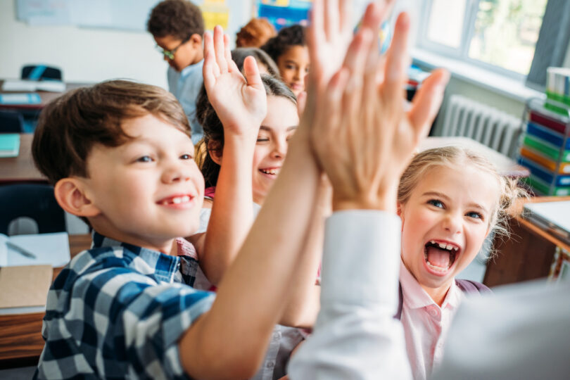 Närbild på elever som ger high five till läraren.