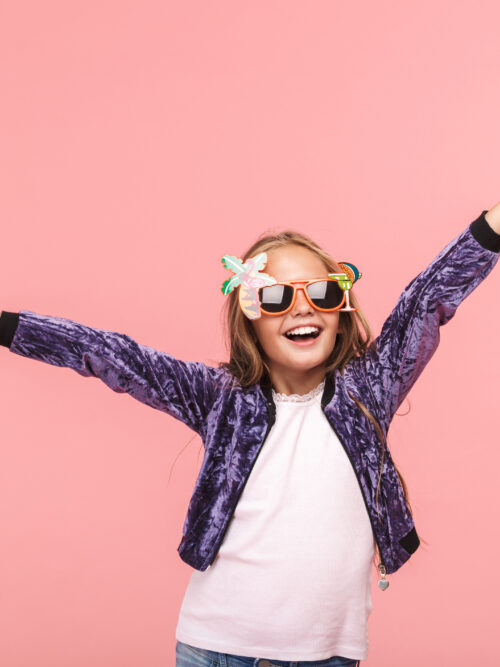 Porträtt av en ung tjej i lekfulla glasögon med rosa bakgrund.