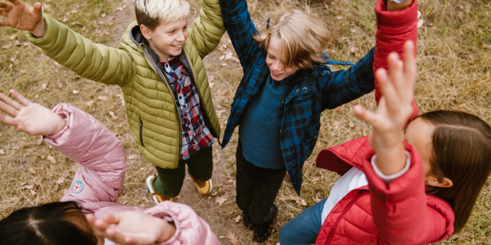 Fyra glada skolbarn tillsammans i en grupp höjer sina händer ovanför huvudet.