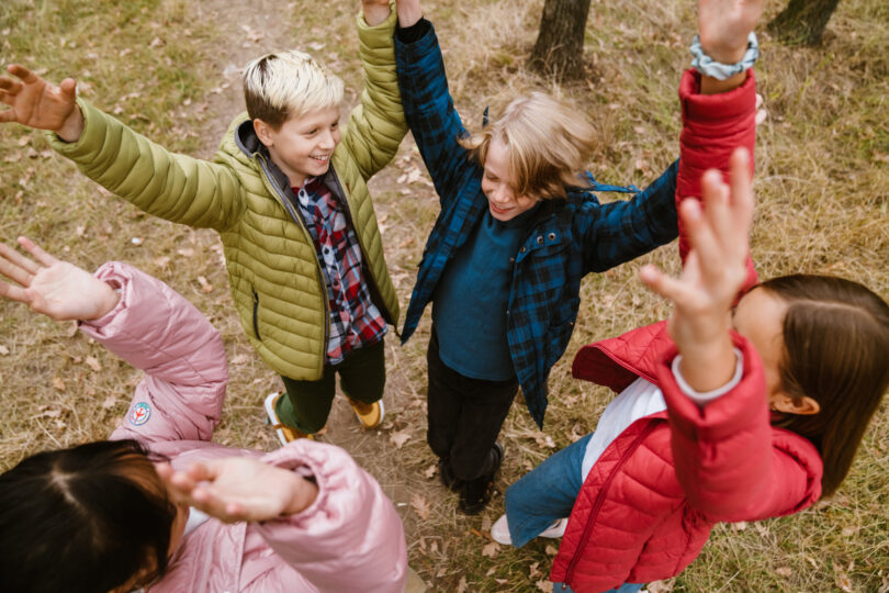 Fyra glada skolbarn tillsammans i en grupp höjer sina händer ovanför huvudet.