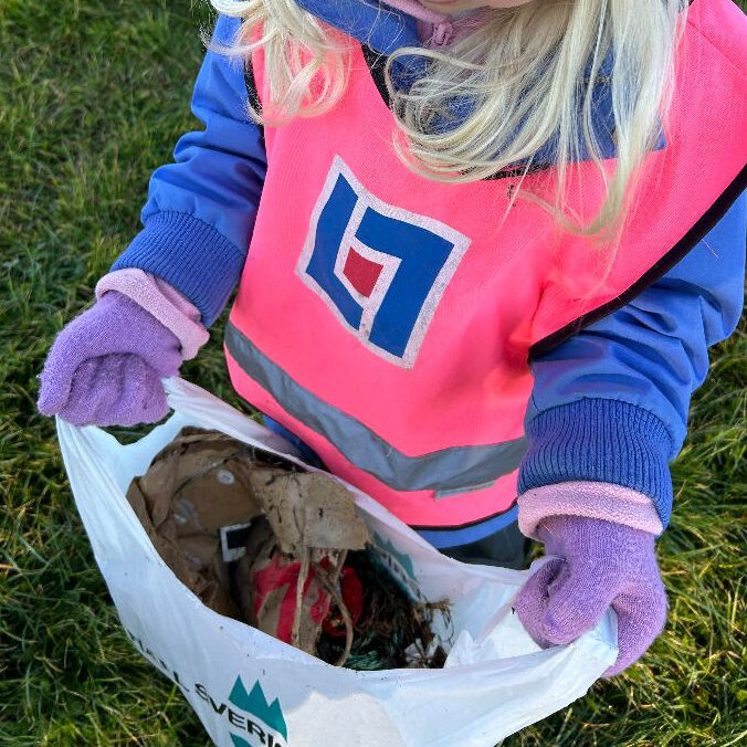 Förskolebarn i rosa varselväst med en påse full med skräp i händerna.