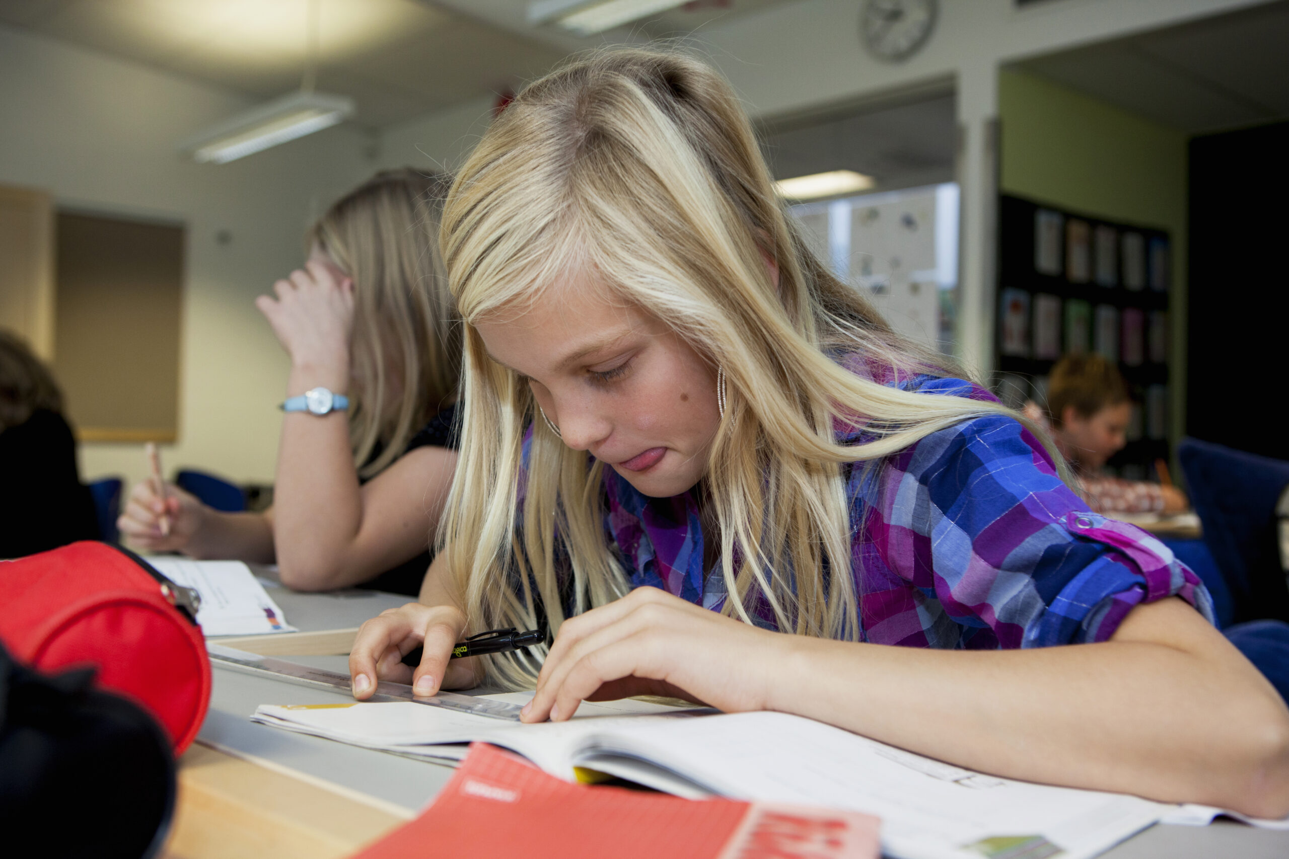 En flicka i 10-årsåldern sitter böjd över en bok på en klassbänk.