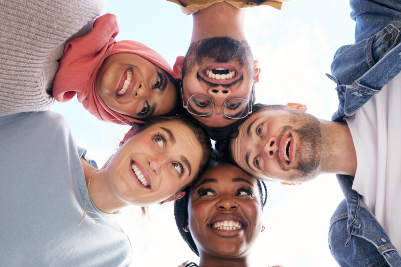Fem personer står i en cirkel med sina huvuden mot varandra.