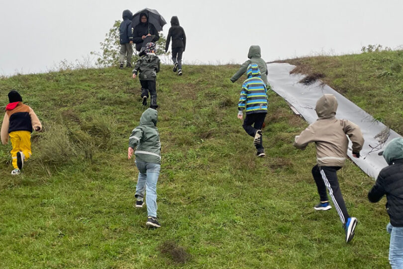 Barn springer uppför en kulle i regn.