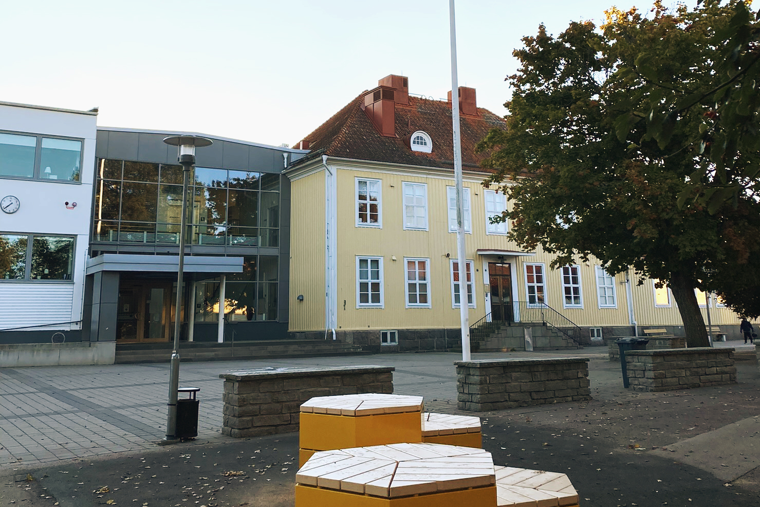 TVå skolbyggnader som sitter ihop, en gul i trä och en med stora fönsterpartier.