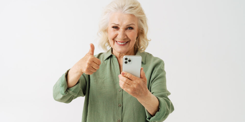 Äldre kvinna som glatt visar tummen upp och håller i en telefon.