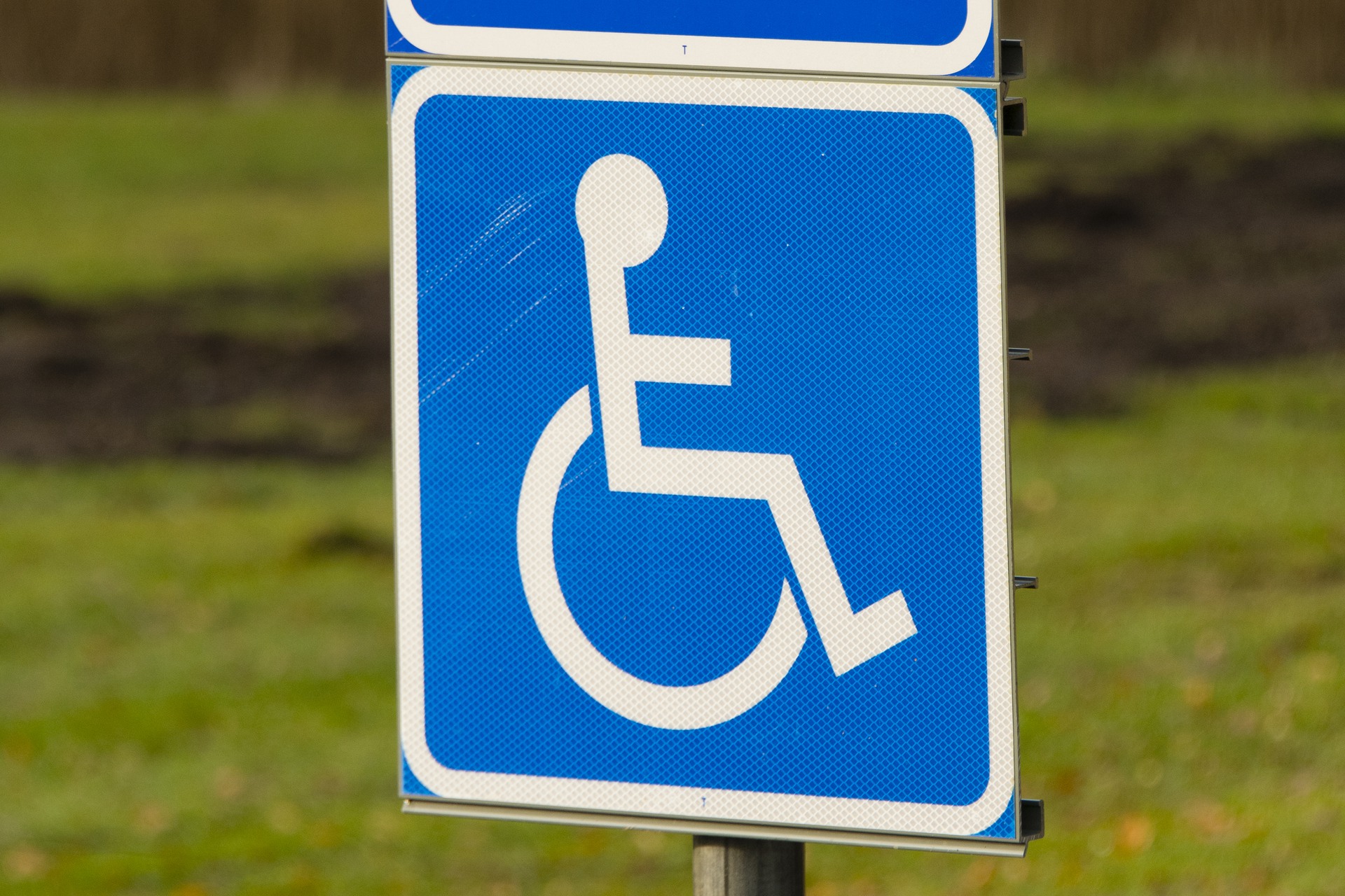 En parkeringsskylt tillsammans med en blå skylt med en vit rullstolssymbol.