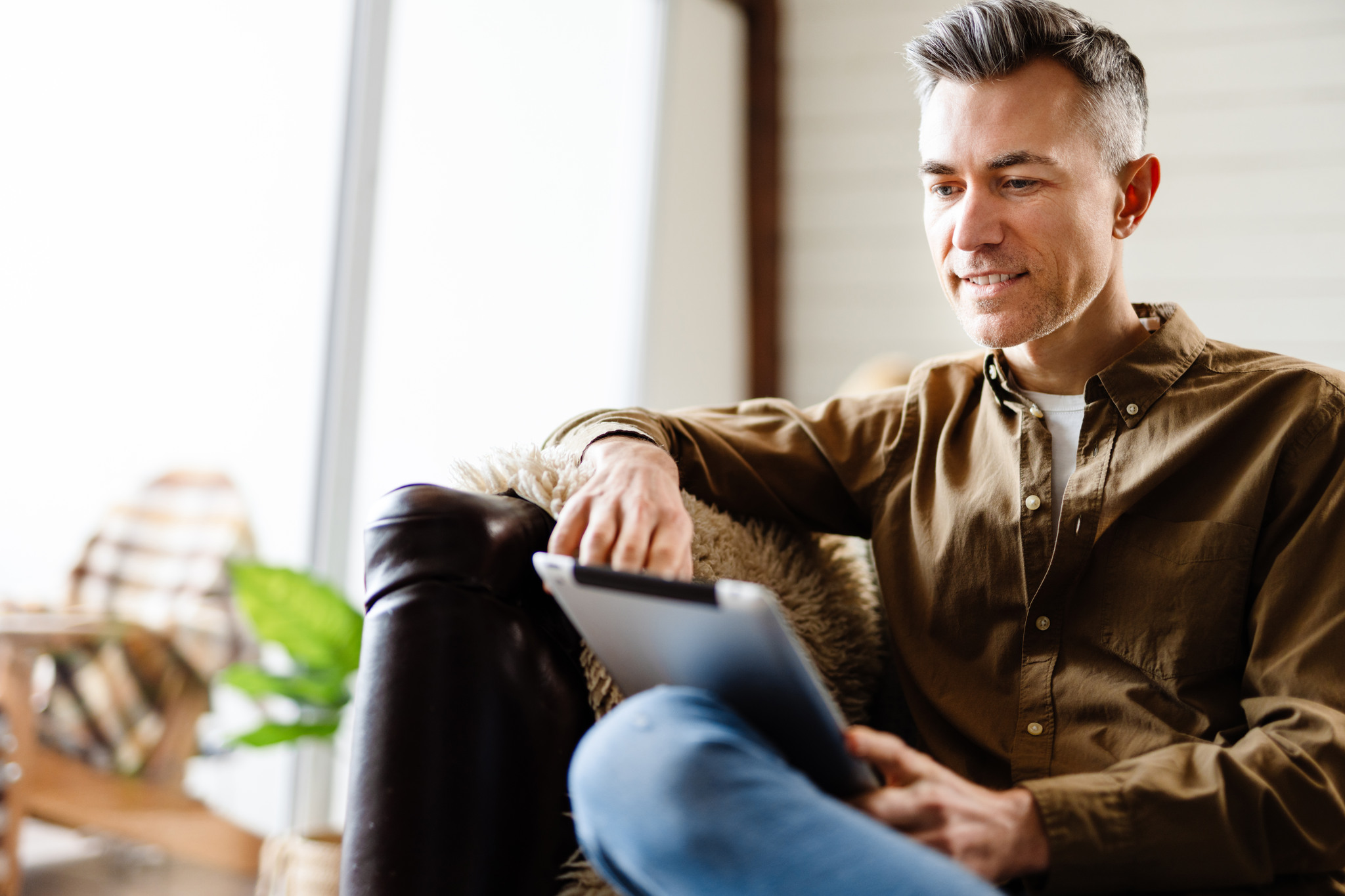 En leende man sitter i soffan med en laptop i knäet.