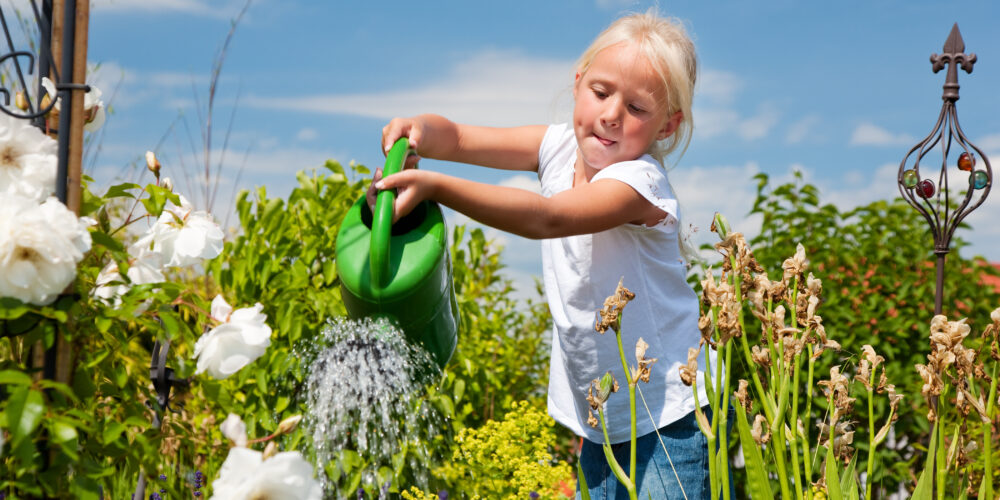 Flicka vattnar en prunkande sommarträdgård med vattenkanna.