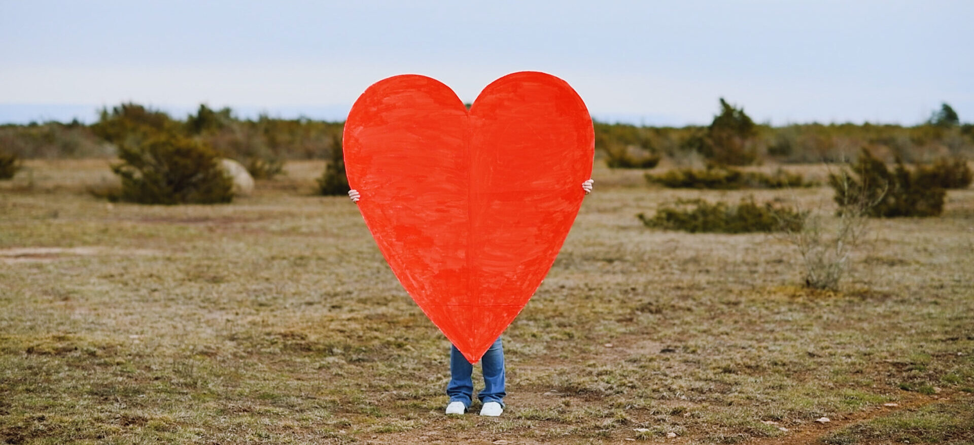 Ett barn står på alvaret och håller upp ett stort rött hjärta.