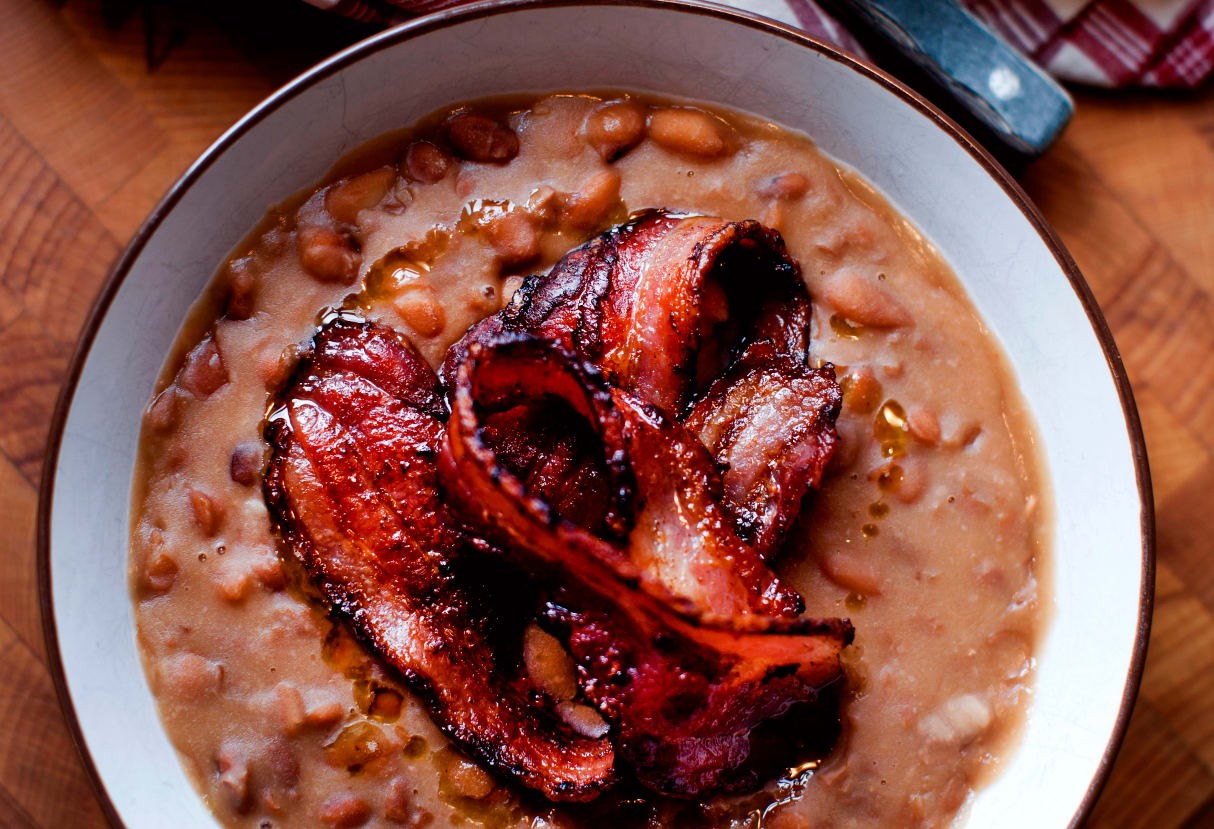 En portion bruna bönor med fläsk på en vit porslinstallrik.