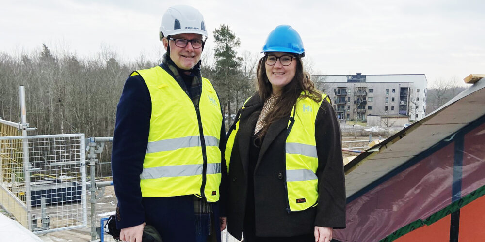 Två personer i byggarbetsplatshjälm och väst står på taket av ett nybyggt äldreboende.