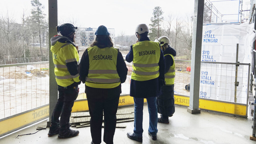 En grupp personer med byggarbetsplatsväst och hjälm står och inspekterar en byggarbetsplats.