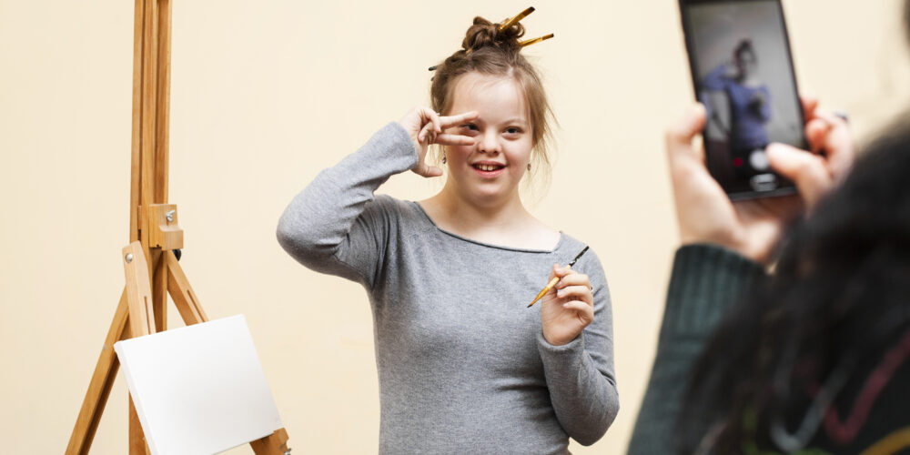 En ungdom står framför ett staffli och målar samtidigt som hon gör en pose och blir fotograferad