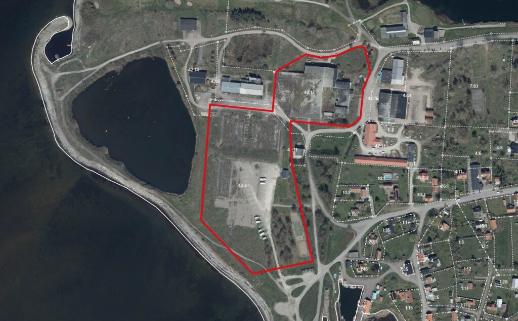Flygbild över ett kustområde där en fastighet markeras med röd linje runt byggnader och öppna ytor. Vitstreckade tomtgränser och nummer syns, bland annat 42:12, 42:5, 42:11 och 42:14, intill vägar och bostadskvarter.
