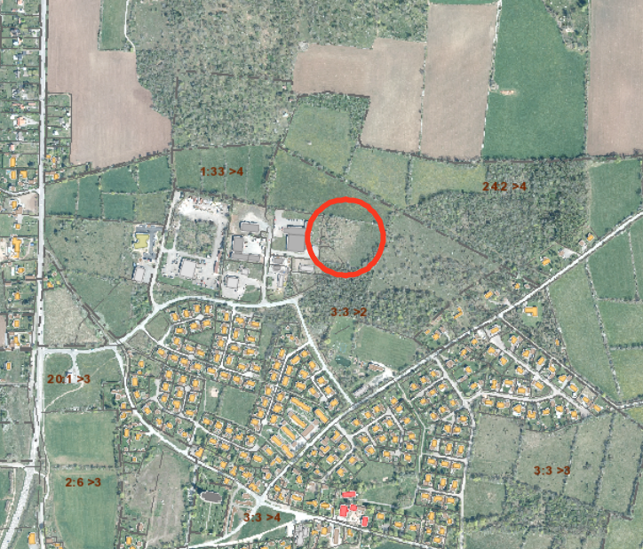Flygfoto över ett bostadsområde och omgivande åkrar och skog, med ett planområde markerat med röd ring vid skogsbrynet nära industribyggnader. Synlig text: “1:33 >4”, “2:42 >4”, “3:3 >2”, “20:1 >3”, “2:6 >3”, “3:3 >4”, “3:3 >3”.
