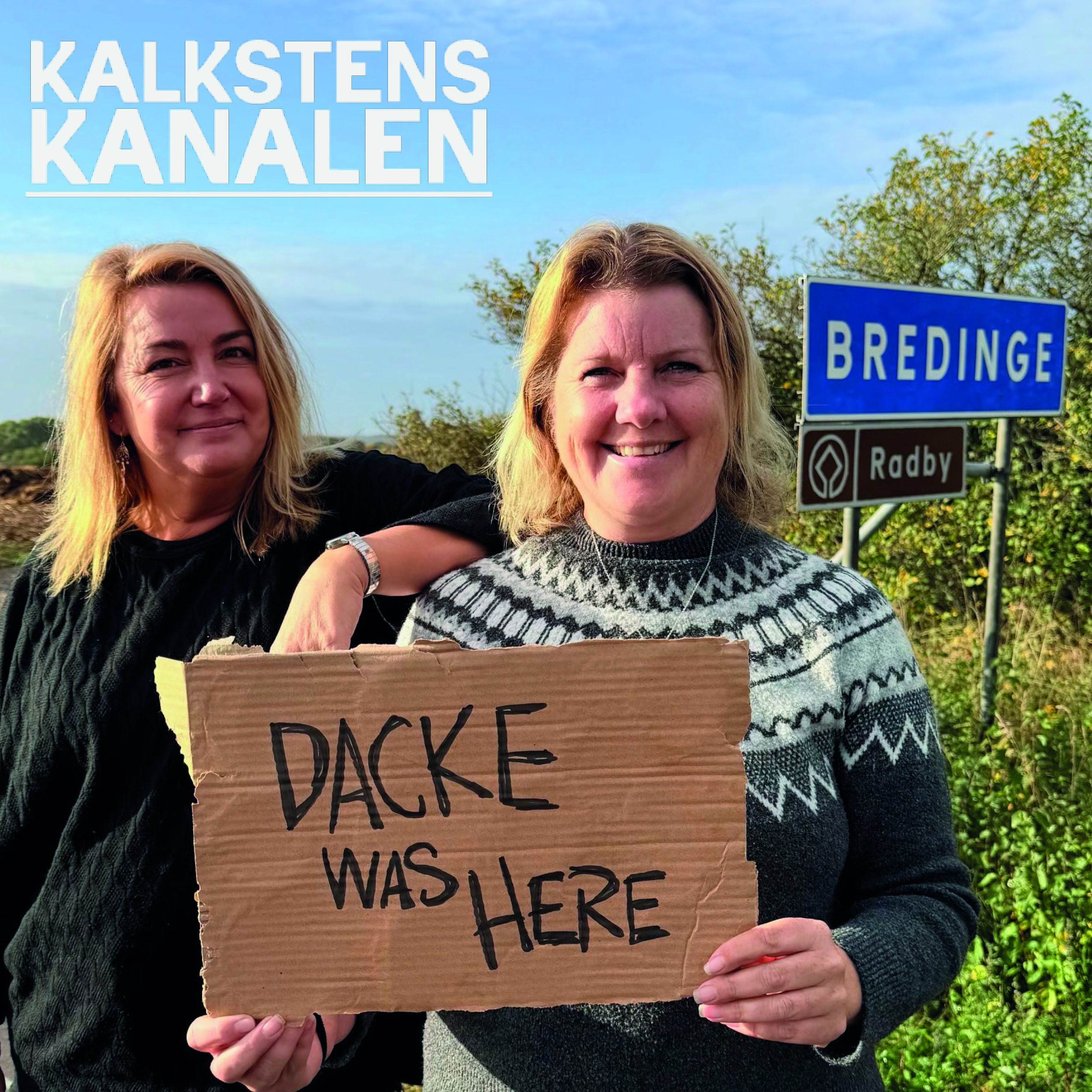 Två kvinnor ler mot kameran vid en vägkant; den ena håller en kartongskylt med texten ”BACKE WAS HERE”. I bakgrunden syns vägskyltarna ”BREDINGE” och ”Radby” samt rubriken ”KALKSTENS KANALEN”.